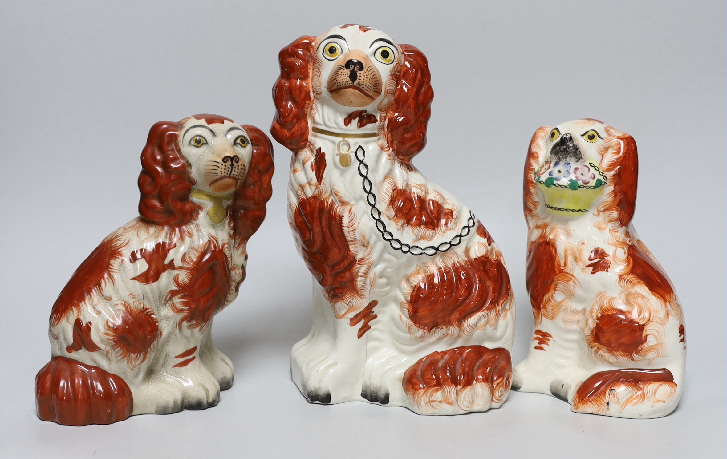Three Victorian Staffordshire pottery dogs, one holding a basket of flowers from its mouth, the largest 24.5cm high
